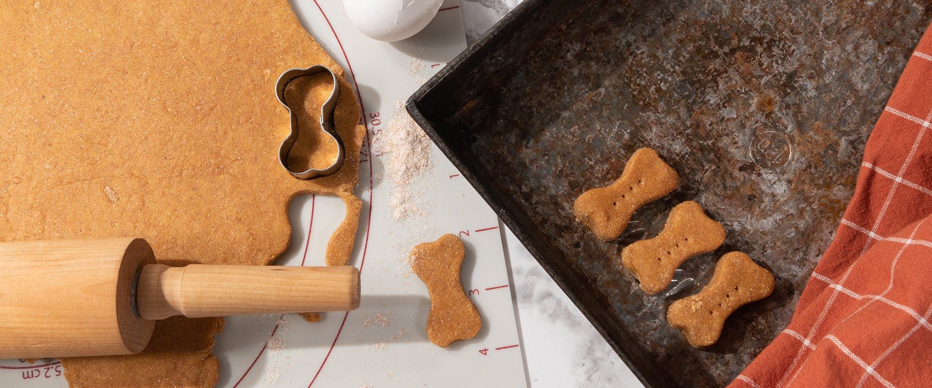 A rolling pin and a baking tray with bone-shaped dog biscuits 