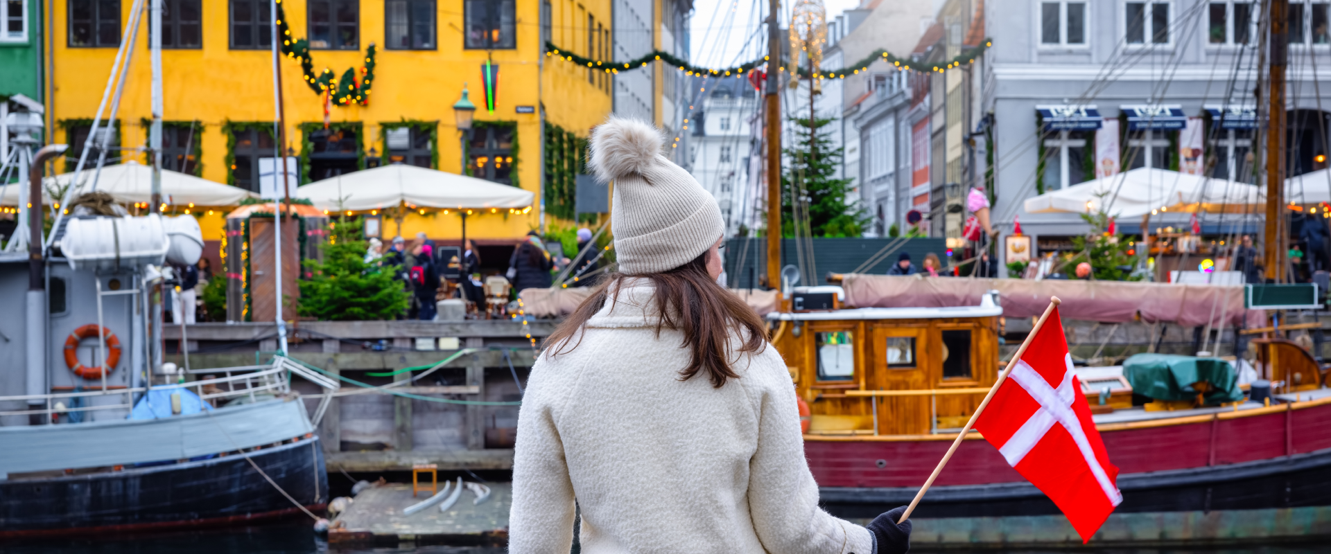 a solo female traveler on the docks of Copenhagen holding a Danish flag