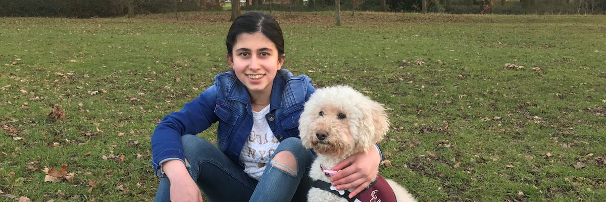 A girl sitting down in the park with her arm around a dog