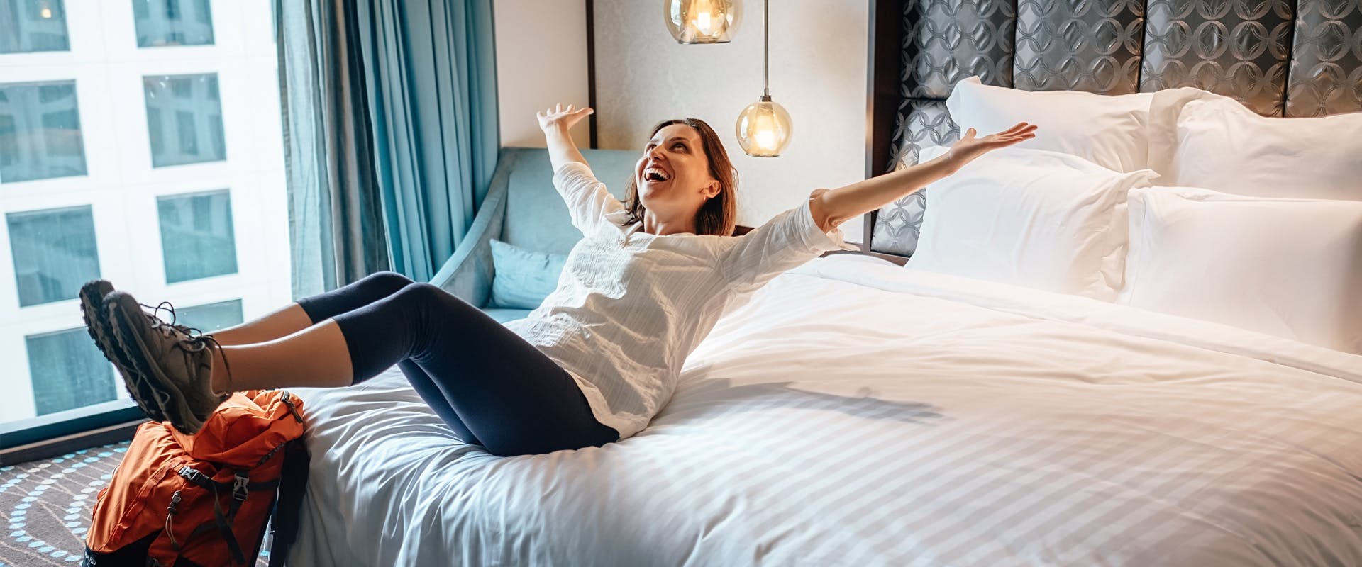 A woman sits on a hotel bed.