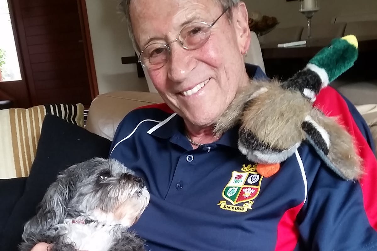 A man smiling at the camera, holding a dog who is looking up towards his face