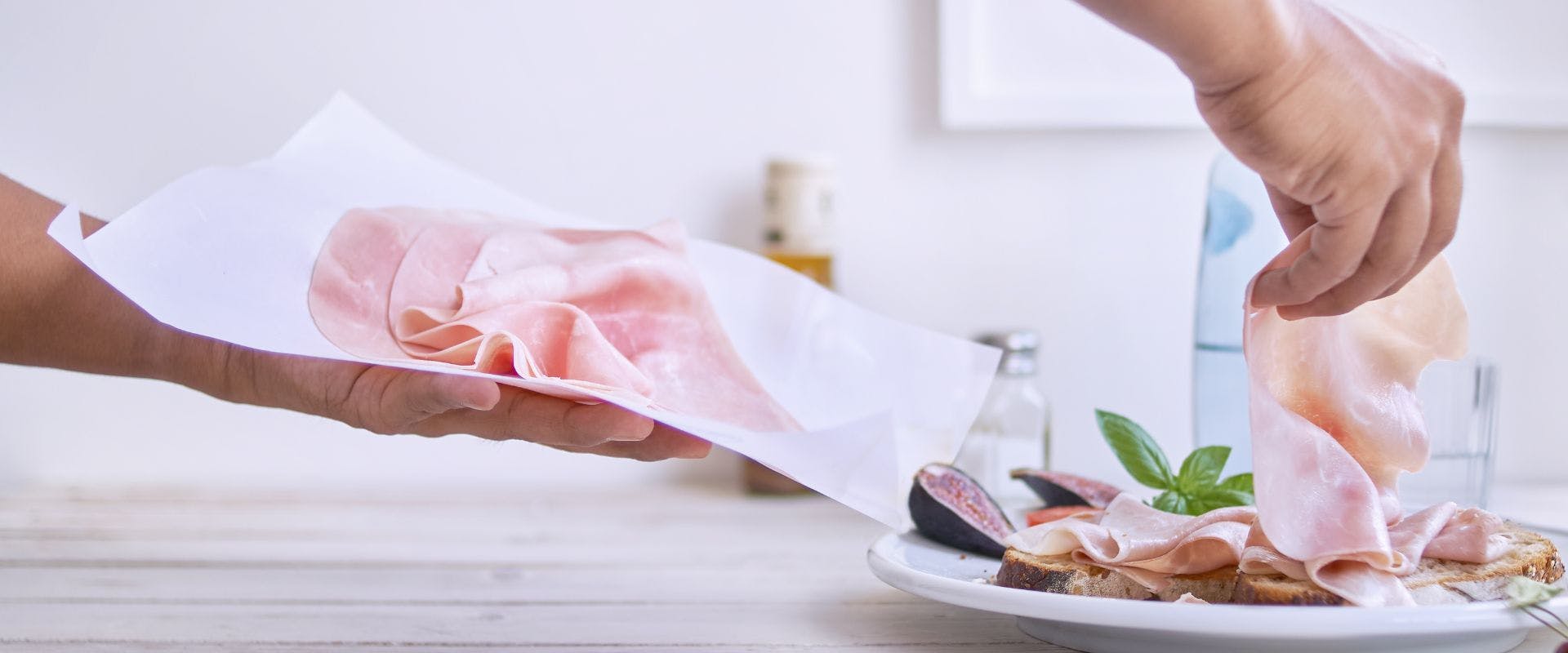 Person laying slices on ham onto a plate