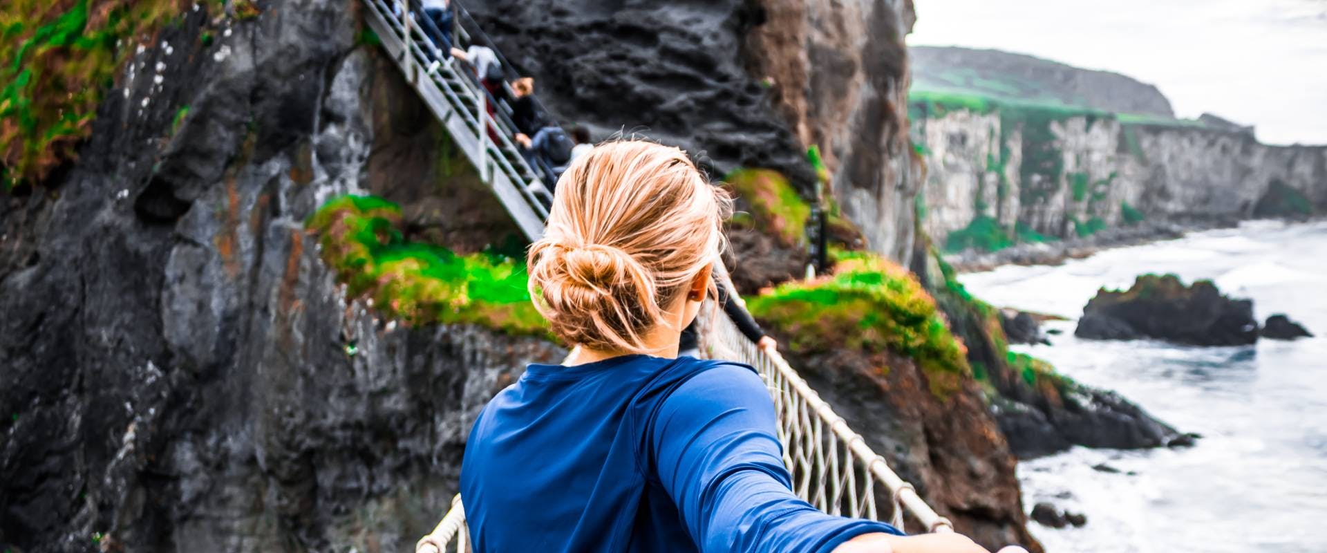 solo female traveler crossing a wire bridge between the cliffs of moher in ireland