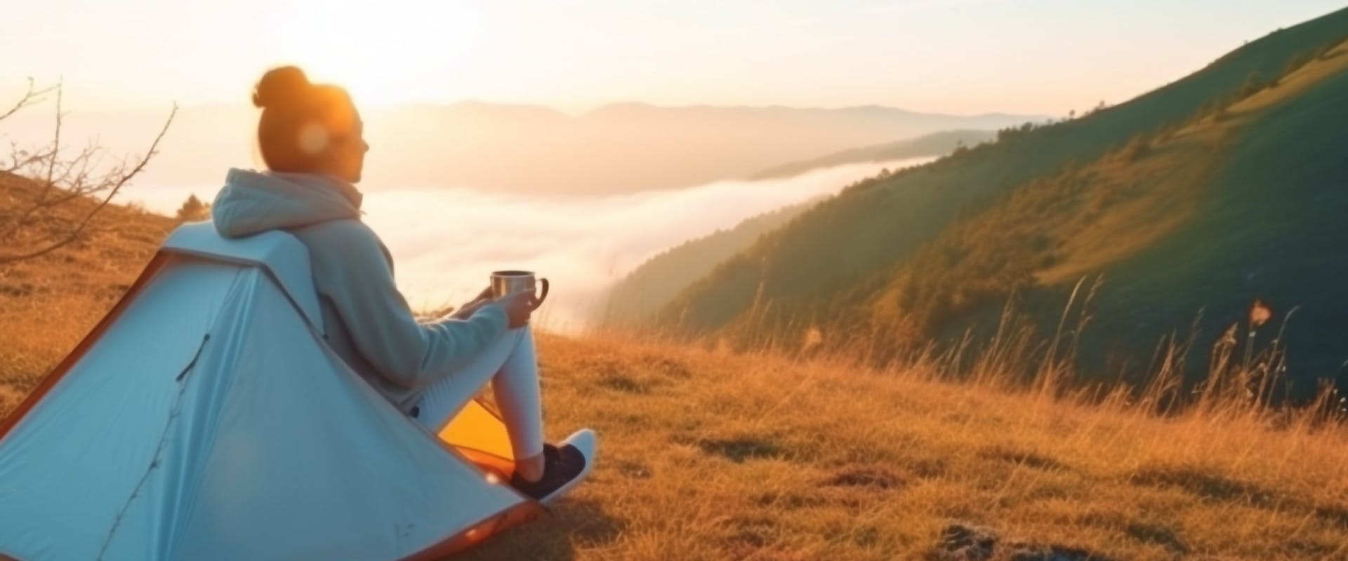 solo female traveler looking out over a valley as the sunrises as she sits in her solo camping tent