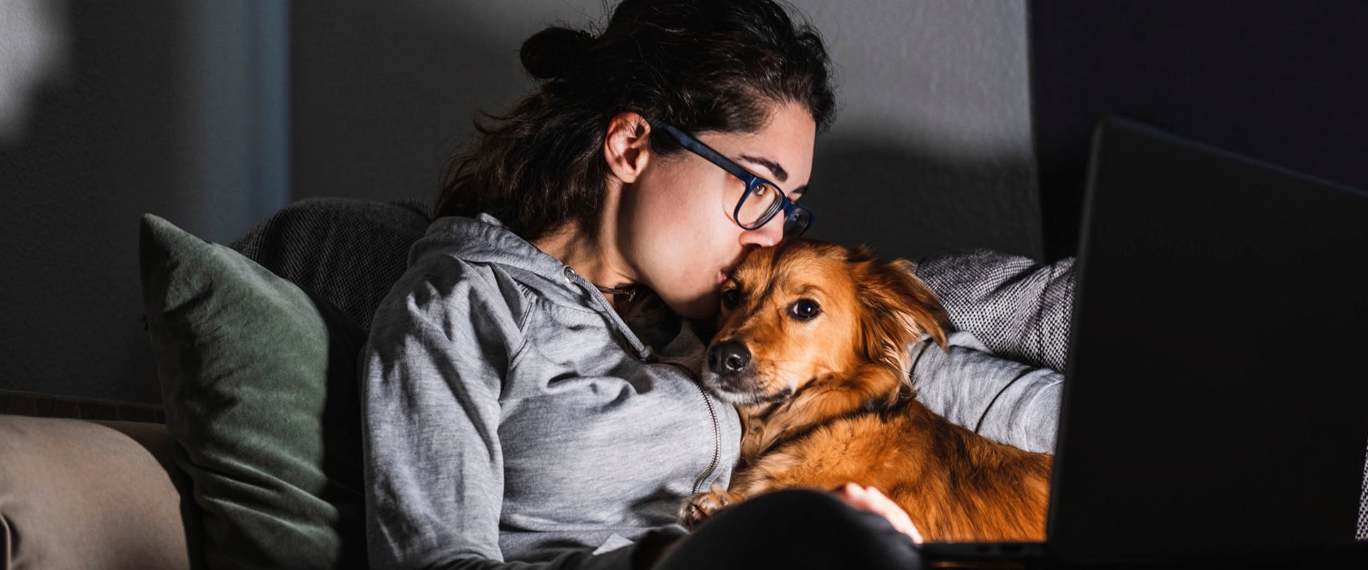 A woman cuddling with her dog while watching a film on her laptop