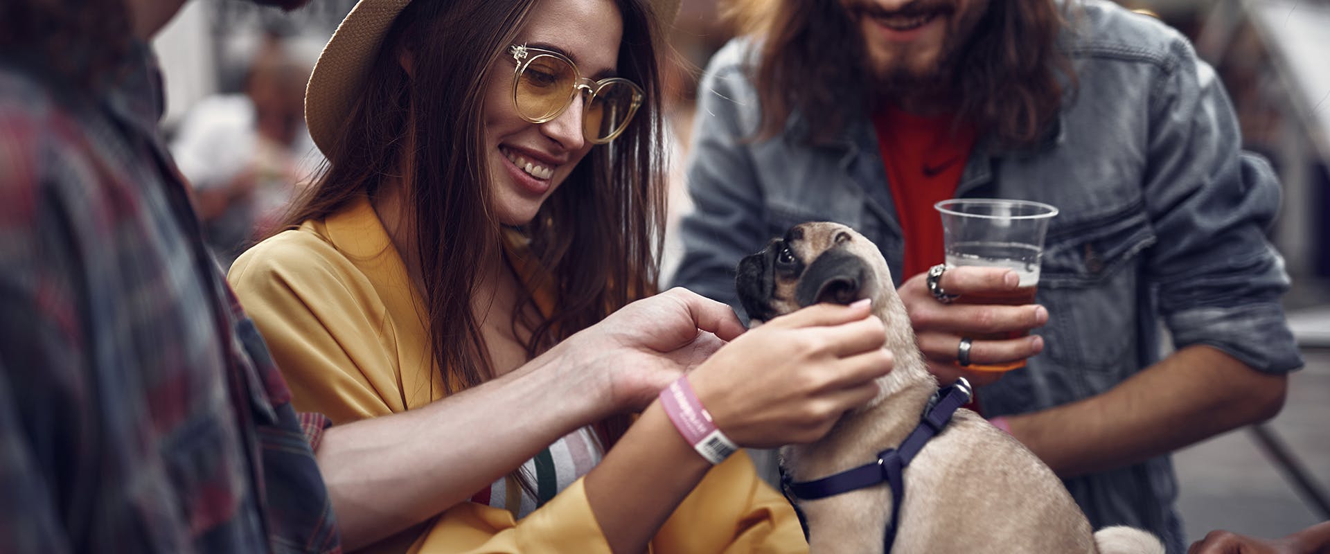 A group of people enjoying drinks and sitting outdoors at a restaurant, stroking a small pug puppy