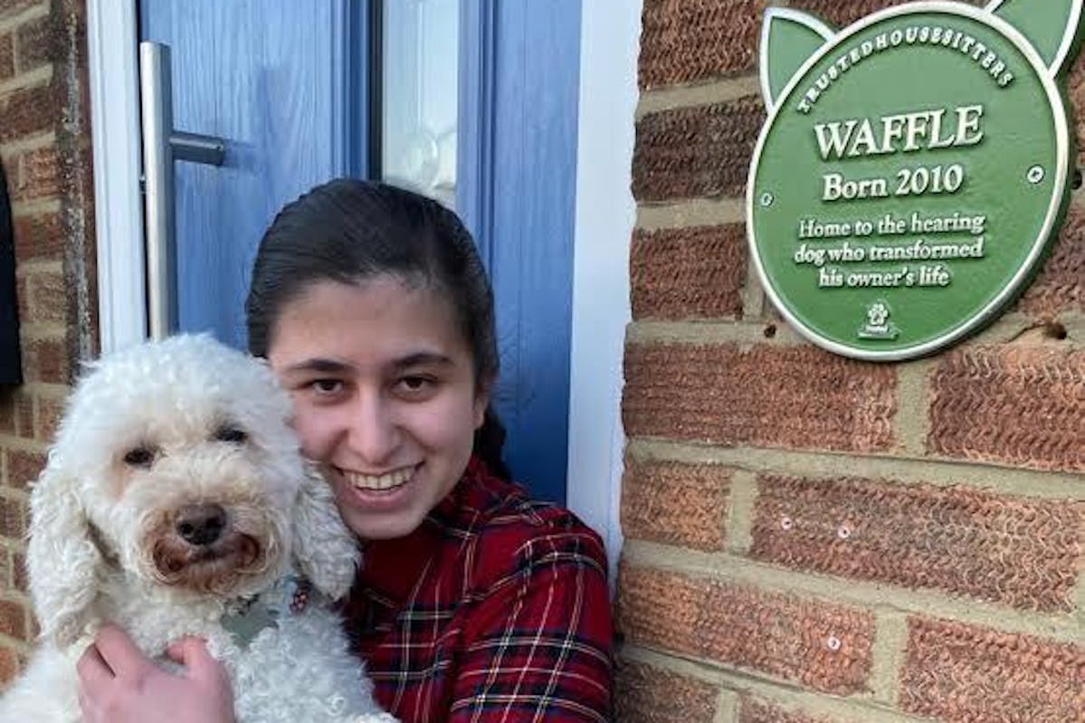 A girl standing outside a house holding a dog in her arms