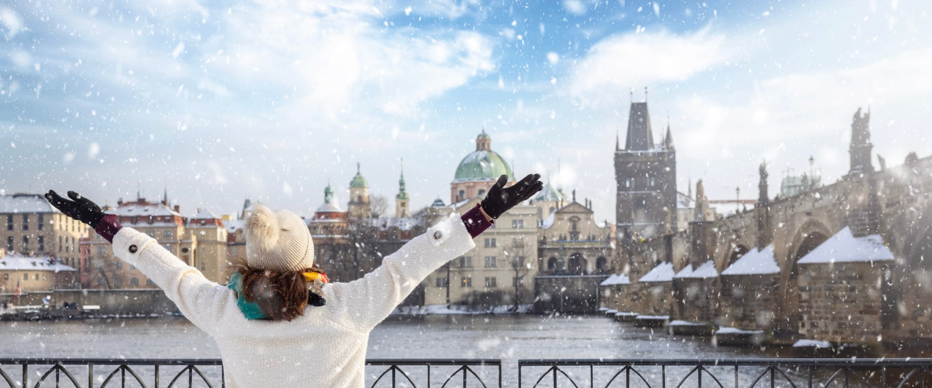 a solo female traveler looking over the Vltava River in winter next to Charles Bridge covered in snow