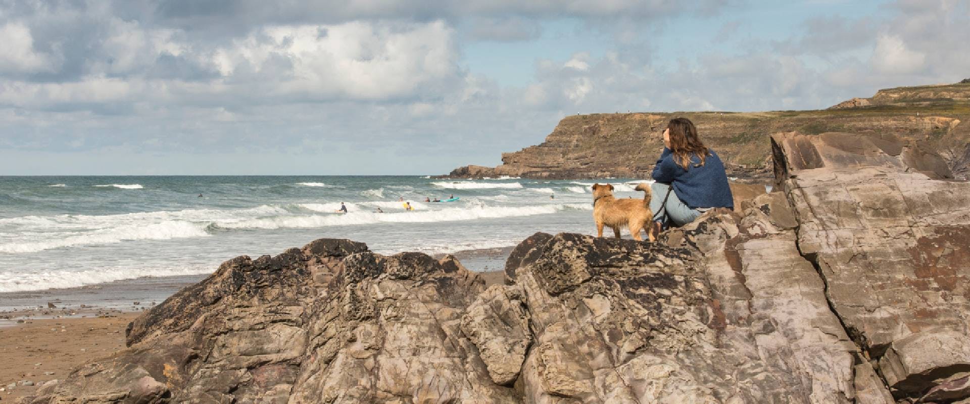 Person and a dog sat on a rock at a beach in Bude, Cornwall