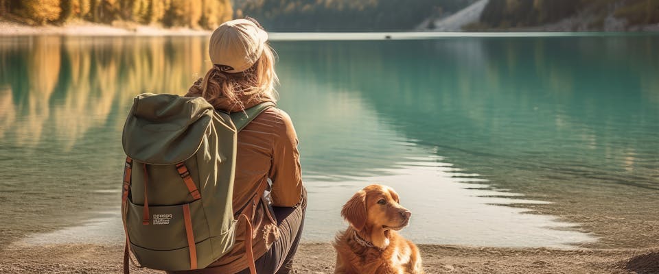 solo female traveler sat by a mountain lake next to a golden retriever