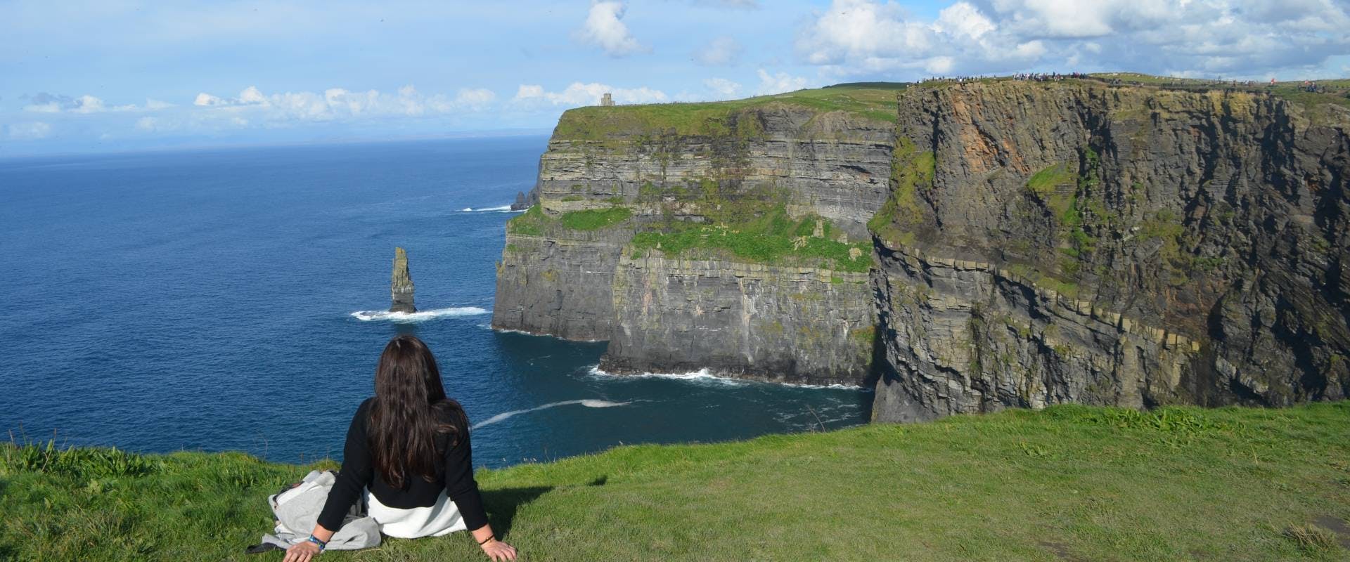 solo female traveler sat on the looking over the cliffs of moher