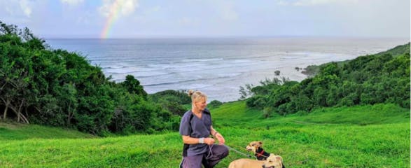 A woman standing by a rainbow, holding two dogs on a leash