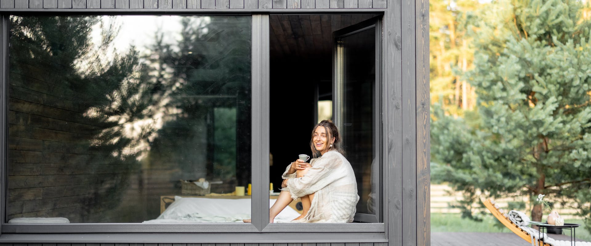 a woman sat in the window of a large wooden rural house in a countryside area