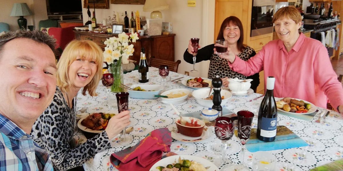 A group of people sitting around a dinner table, raising their glass to the camera