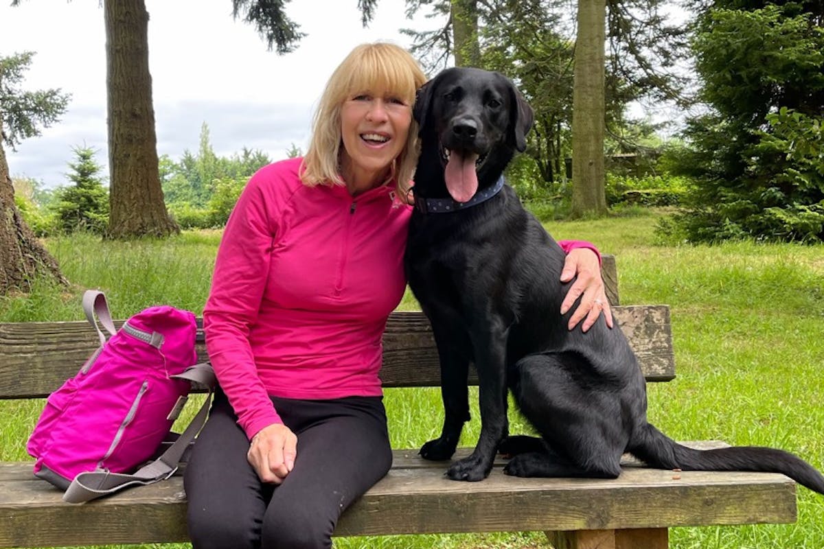 A woman sitting on a park bench with her arm around a black Labrador