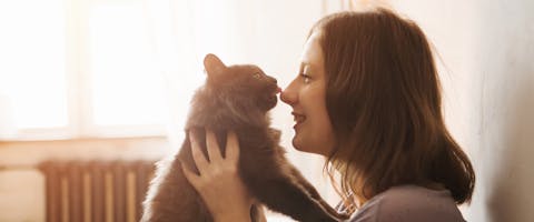 Woman holding up cat to let it lick her nose as a sign her cat loves her.