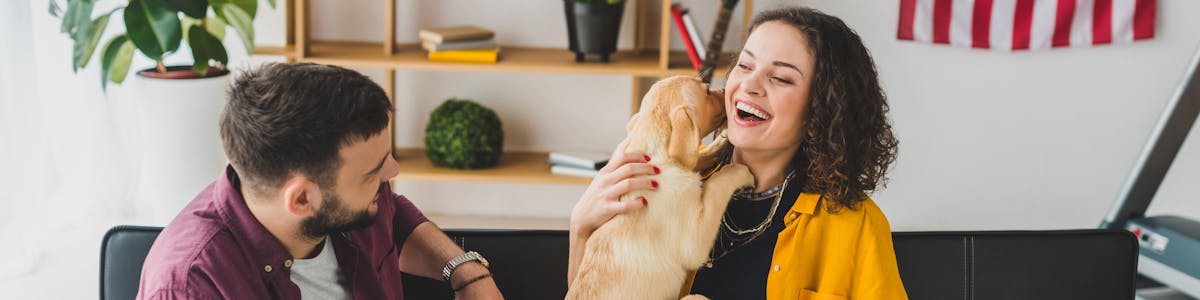 A woman holding a puppy, sitting on the sofa next to a man