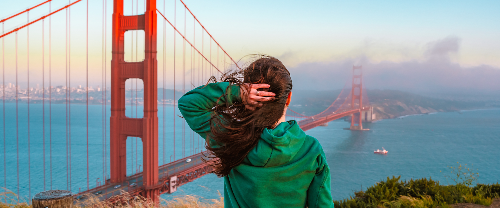 a solo female traveling in a green sweater looking at the Golden Gate Bridge from Golden Gate Park