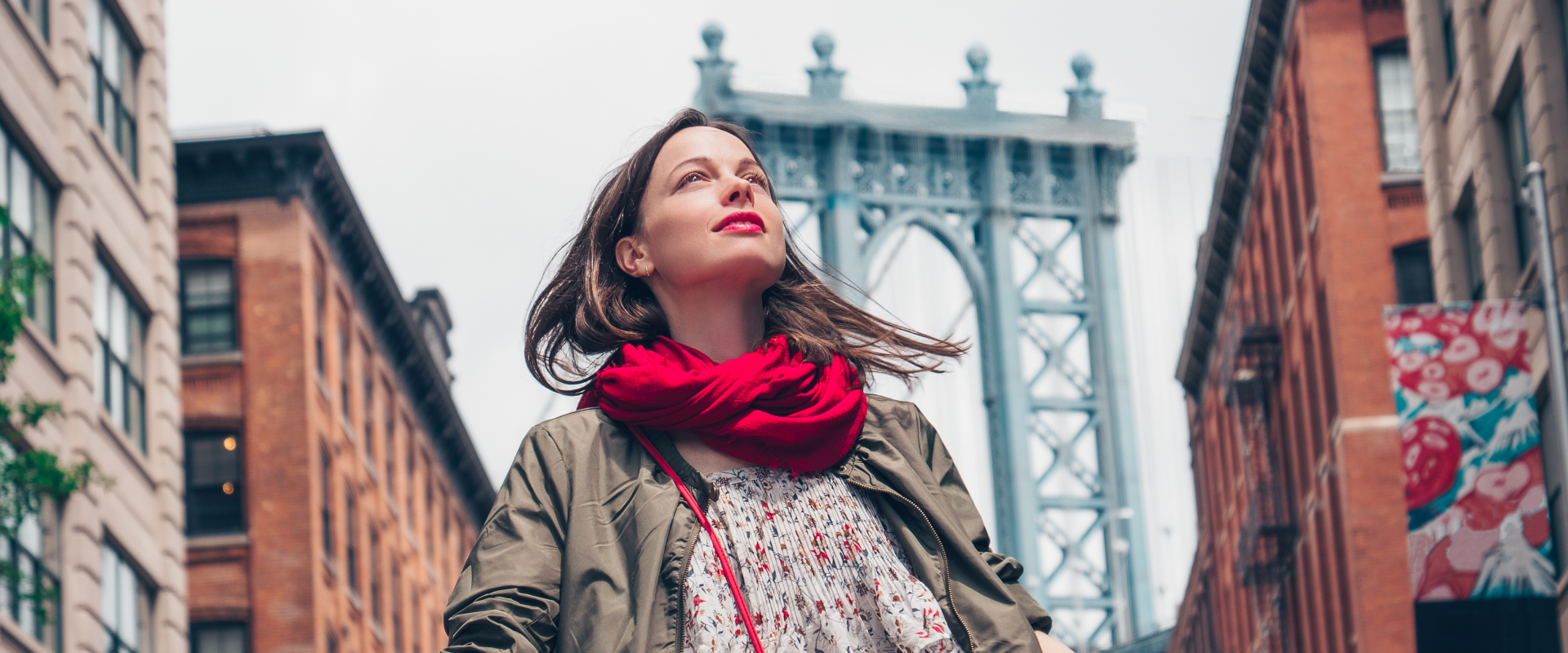 a solo female traveler walking through Brooklyn with the top of the Brooklyn Bridge behind her