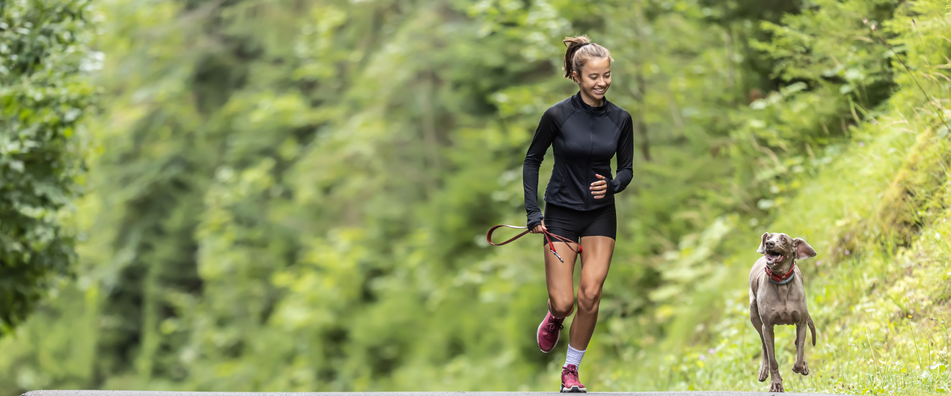 A woman and her dog run through a forest.