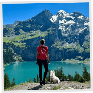 A person and a dog standing in front of a mountain scene