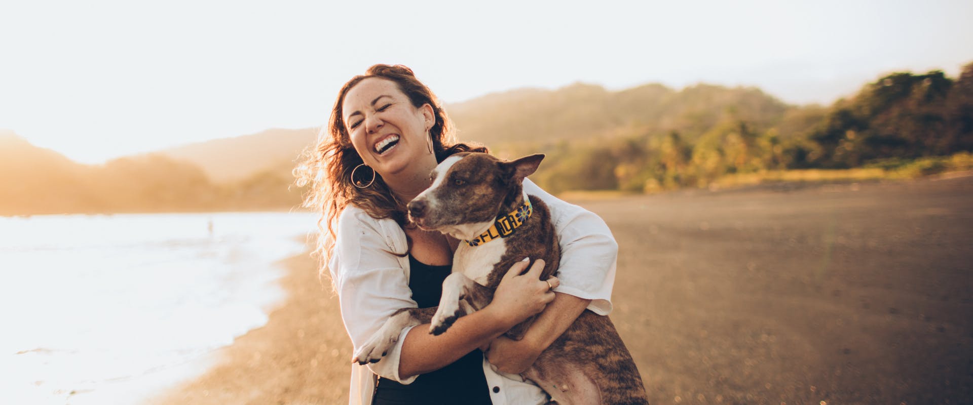 Woman embracing a brown and white dog at a beach