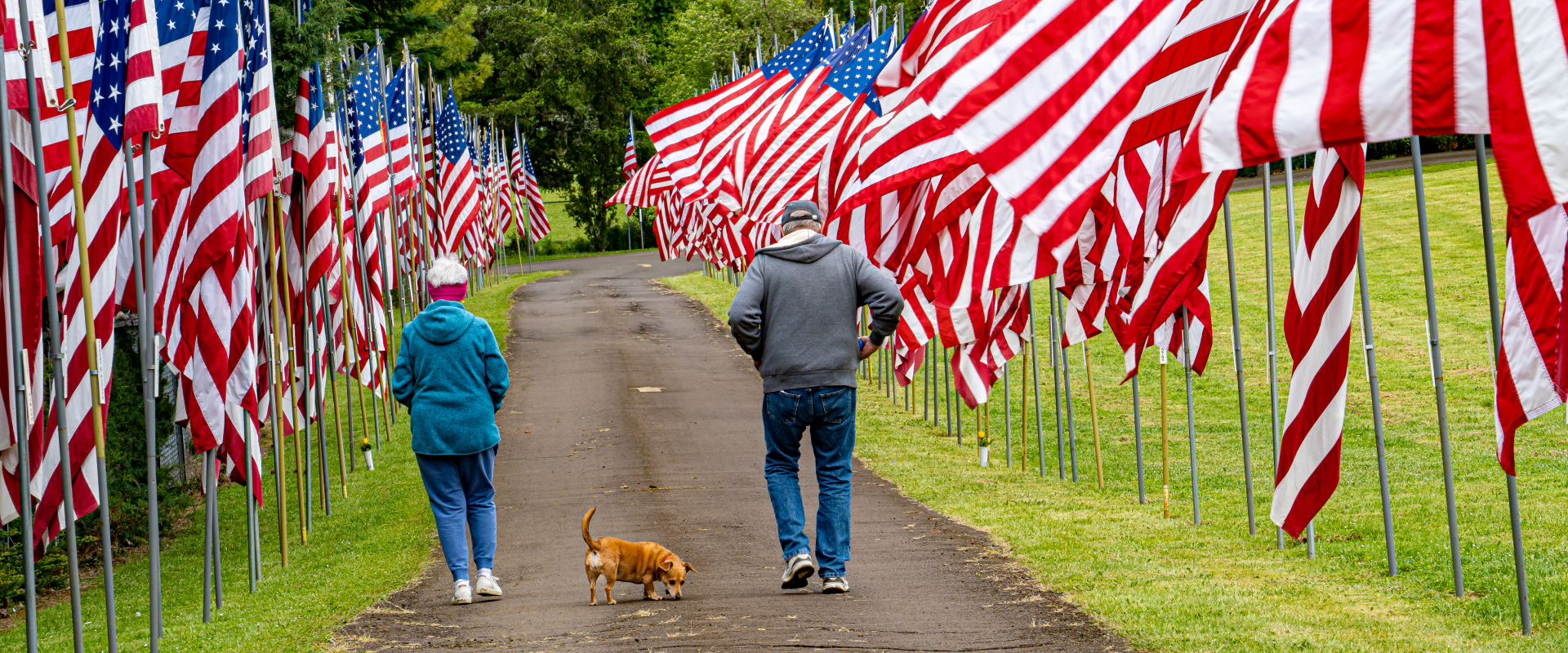 a couple walking a dog through a Dallas park lined with American flags