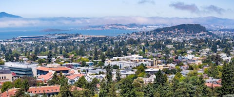 View towards Berkeley, Richmond and the San Francisco bay area shoreline on a sunny day; University of California Berkeley campus buildings in the foreground, California