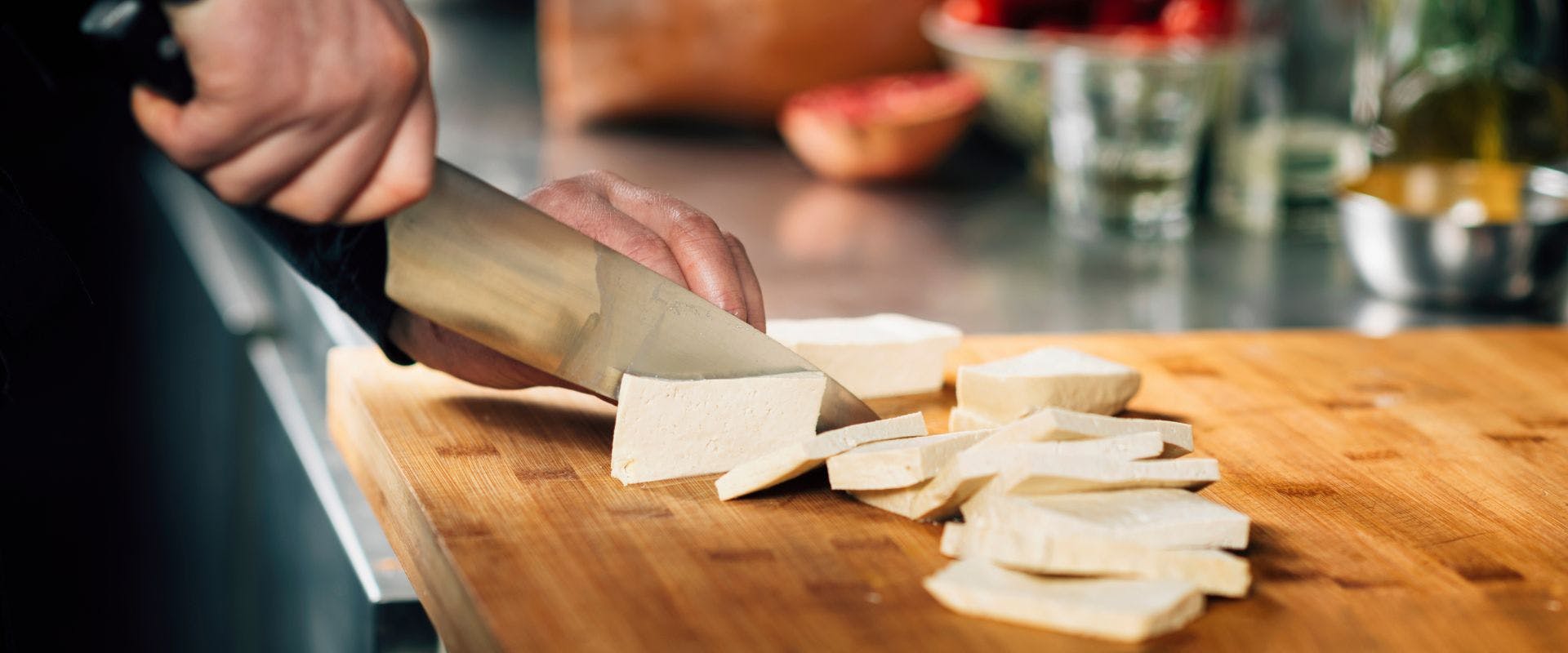 Tofu being sliced on a wooden chopping board