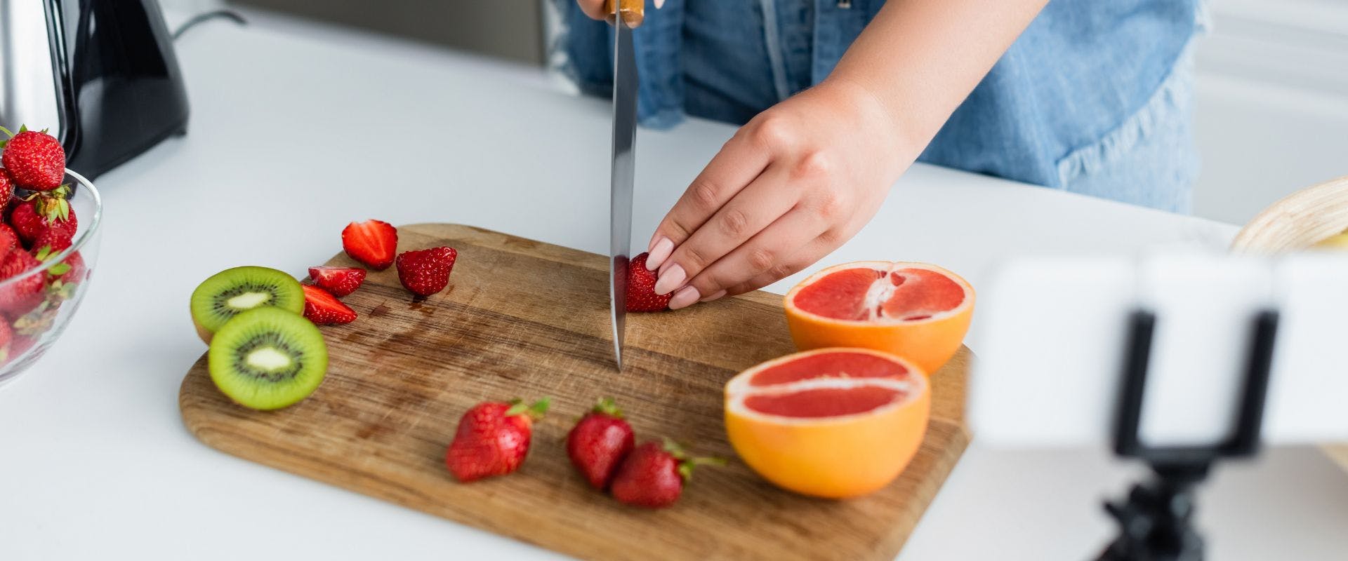 Strawberries being sliced on a wooden chopping board alongside a halved grapefruit and kiwi