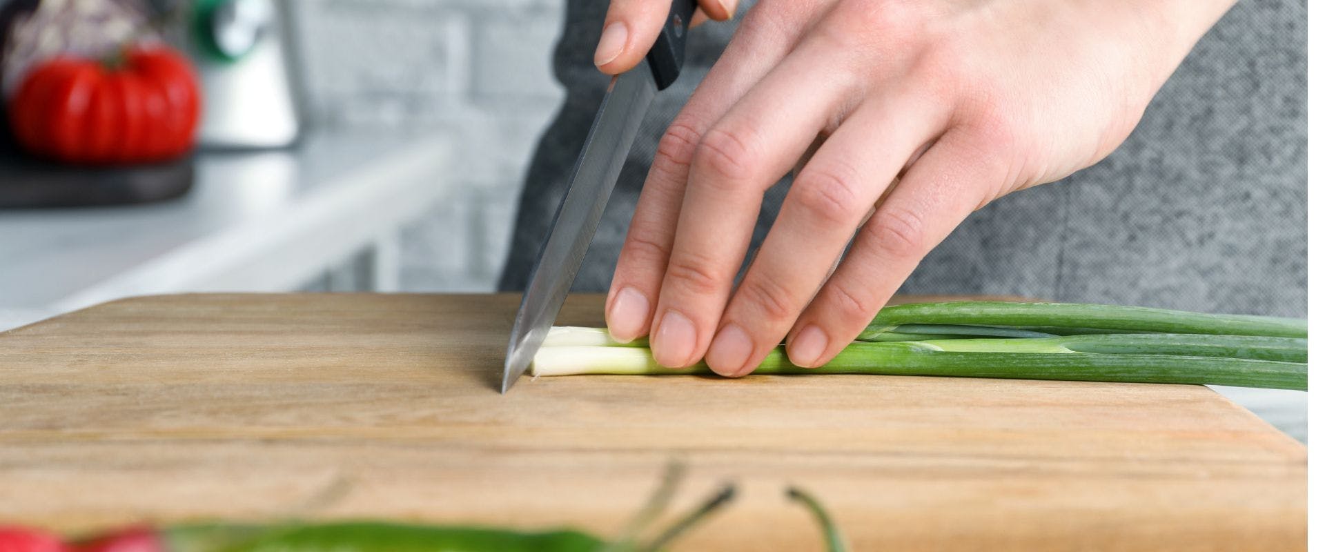 Green onions being chopped on wooden chopping board