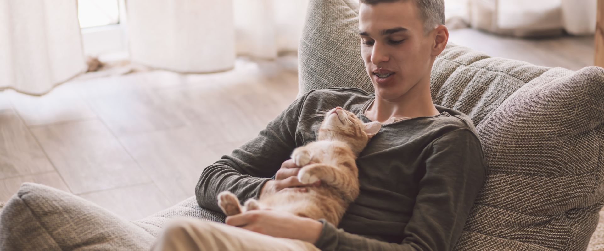 a man reclining on a cushioned gray chair with a tabby cat lying on its back on his chest