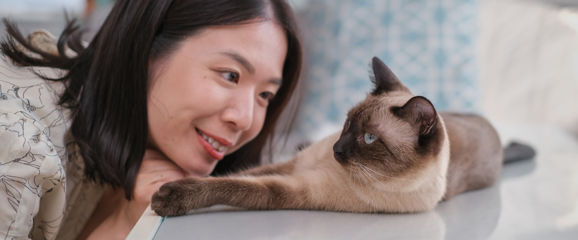 a smiling woman leaning down to face a cat lying on a table top