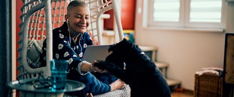 A woman working on a laptop and petting a dog