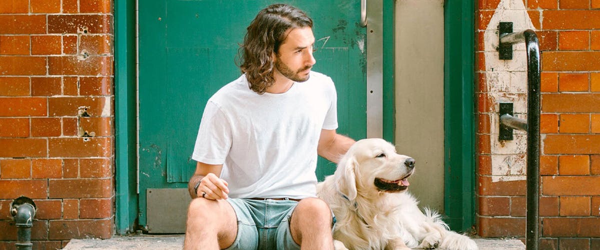 A man sitting on a step outside a doorway, stroking a Golden Retriever