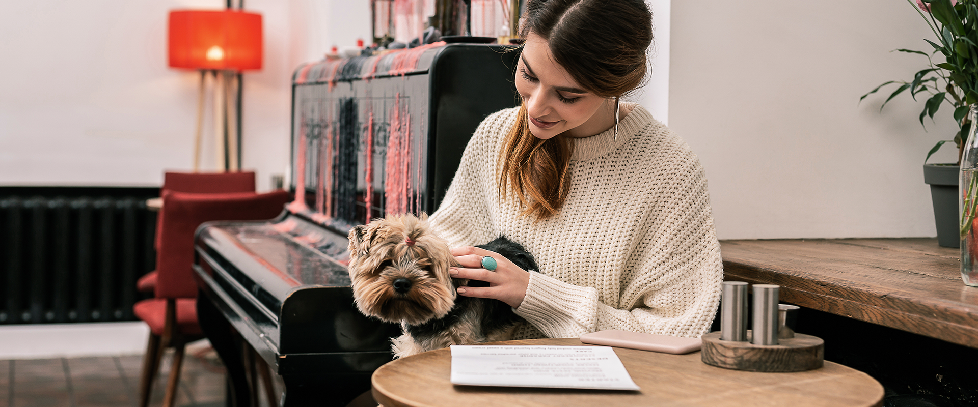 A woman sitting at a table in a cafe with a cute dog sitting on her lap