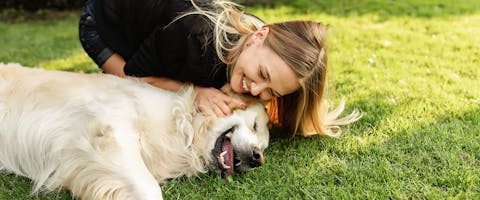 A woman laughing and stroking a dog in the middle of a dog park