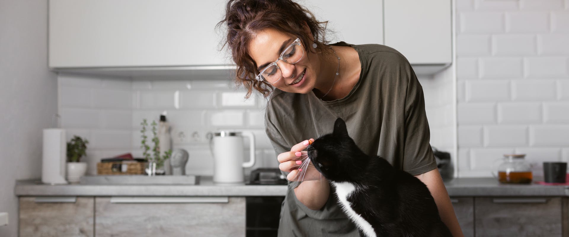 A woman feeding a cat in the kitchen.