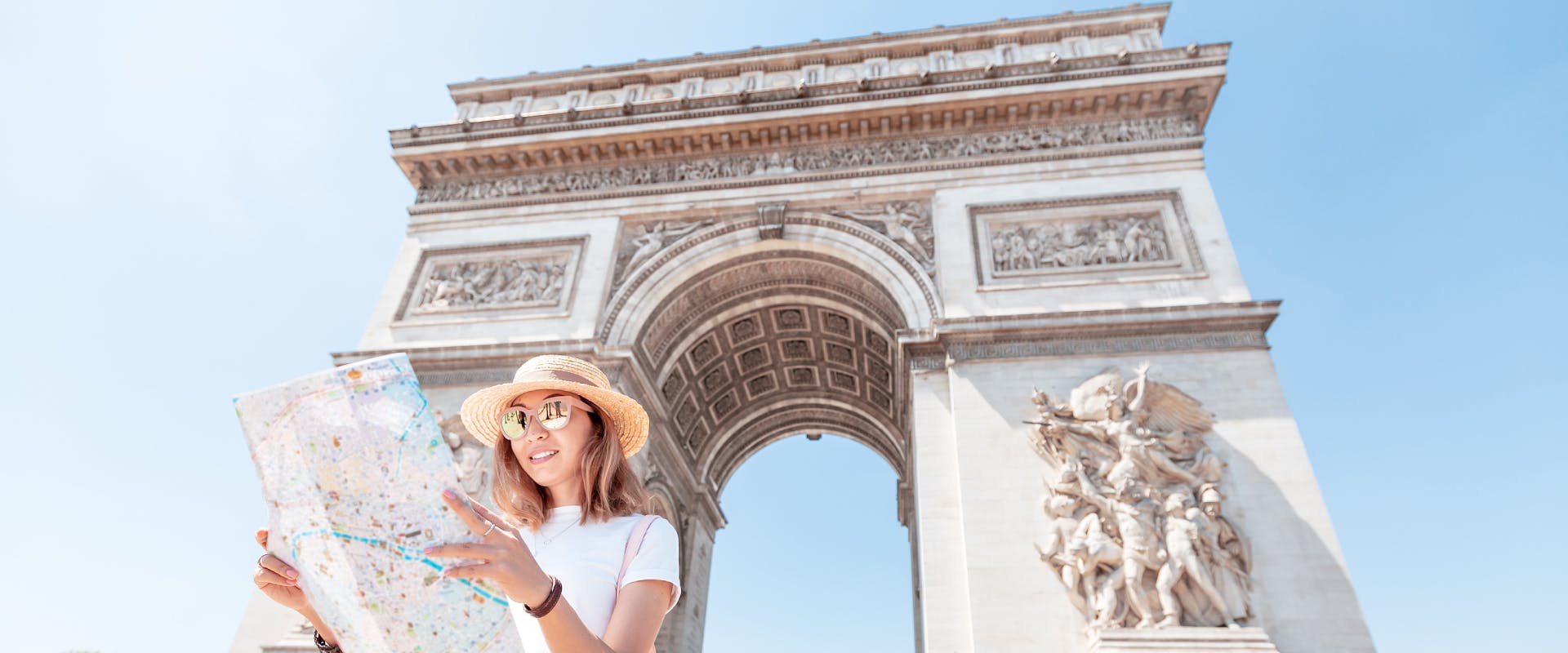 a solo female traveler in Paris standing in front of the Arc D'Triumph whilst looking at a map 