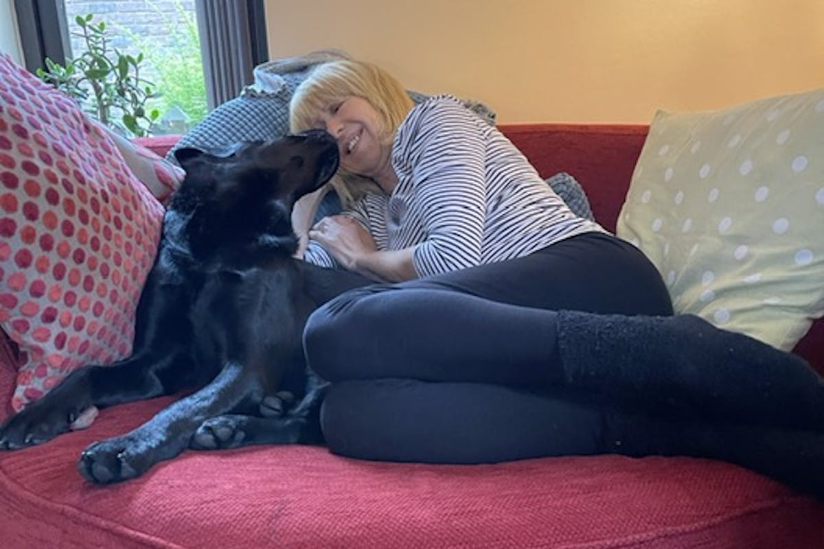 A woman sitting on a red sofa, cuddling with a black Labrador