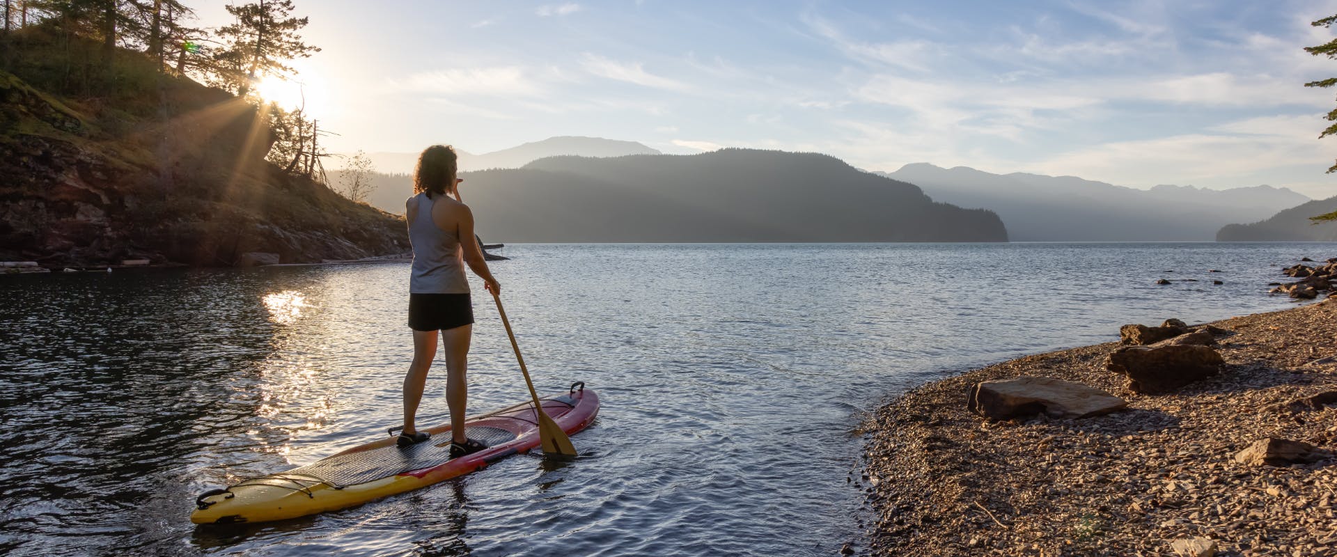 A woman paddle boards across a lake.
