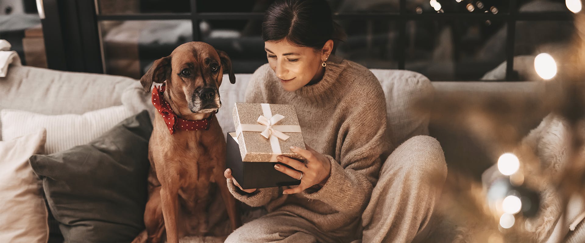 A woman opening a present while sitting on the sofa next to a dog