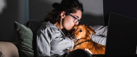A woman cuddling her dog while watching something on her laptop screen