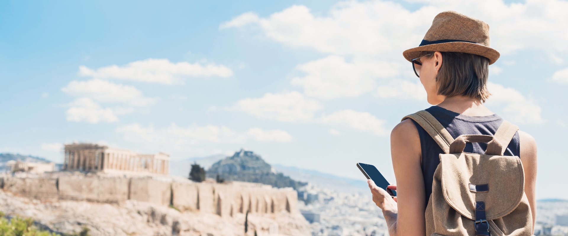 a solo female traveler looking at her phone and the acropolis