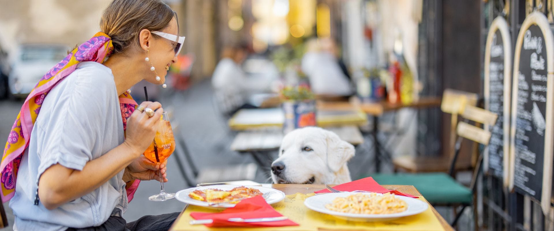 Woman eating Italian pasta while sitting with a dog at restaurant on the street in Rome 