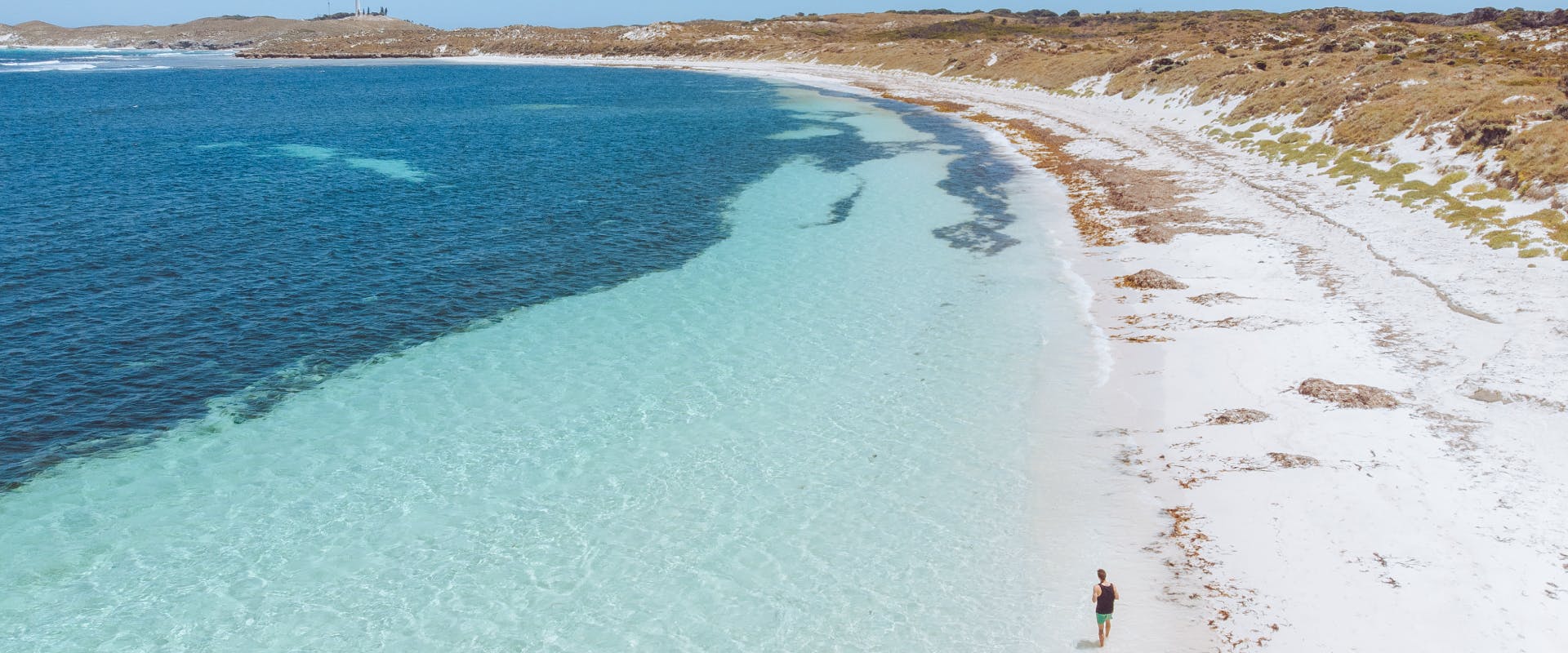 a solo female traveler walking along a white sand beach next to a blue sea in australia