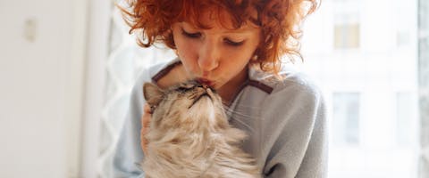 A woman kisses her cat on the head.