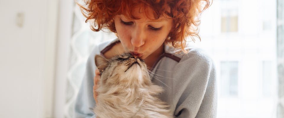 A woman kisses her cat on the head.