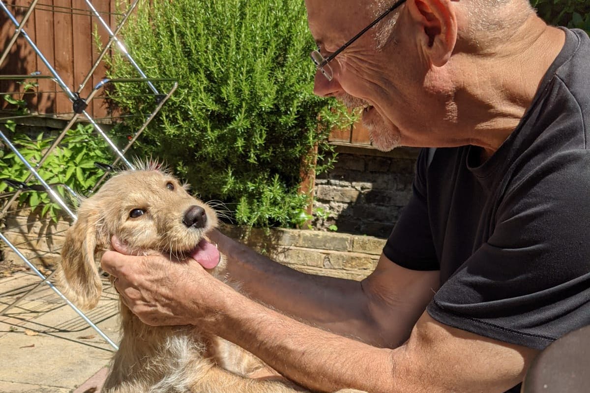 A man sitting outside in a garden holding the face of an excitable puppy