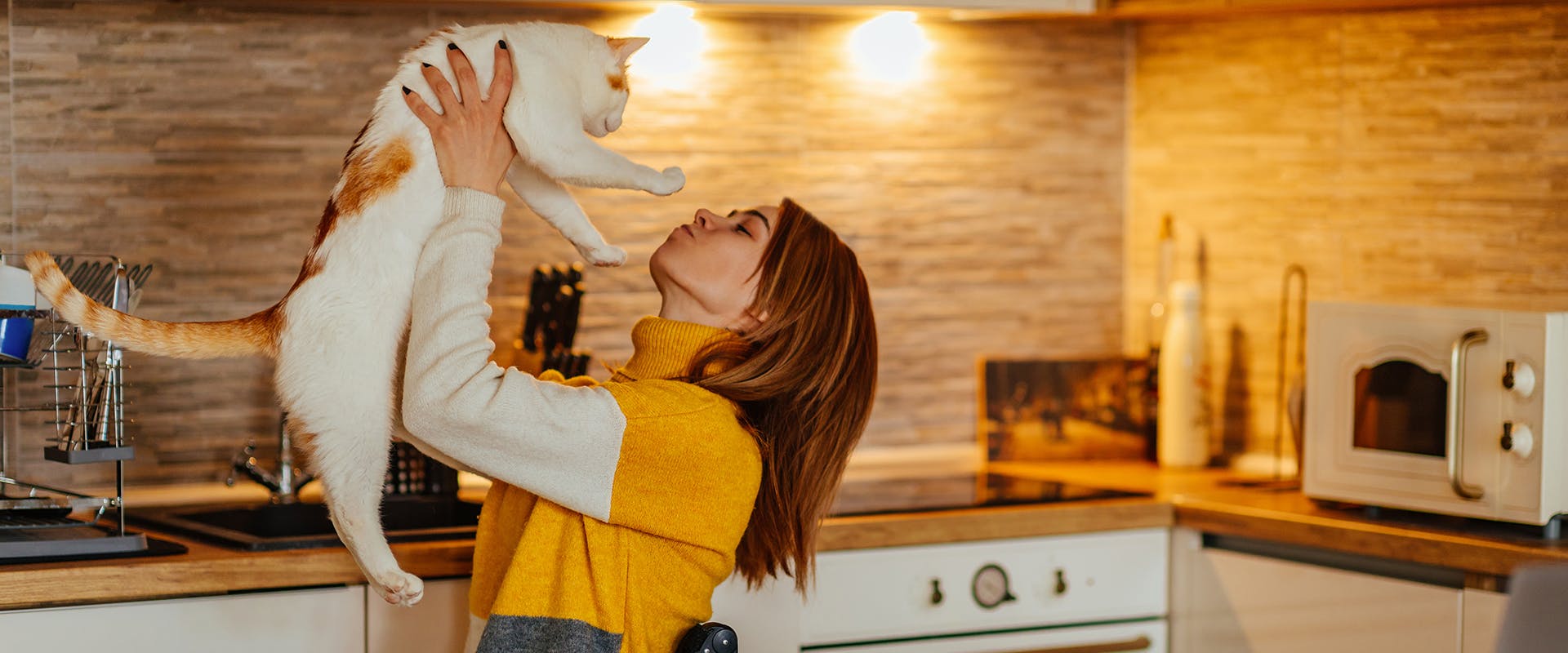 A woman in a kitchen holding up a white and ginger cat